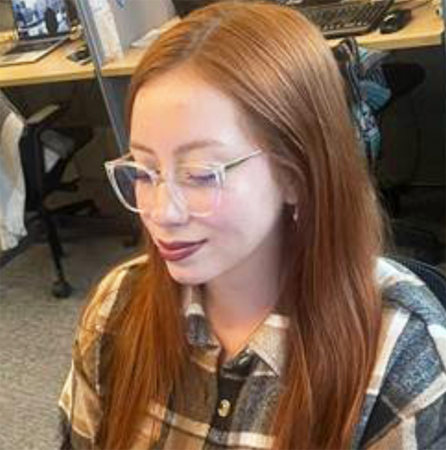 Red-headed woman with glasses looking down at a screen with a slight smile