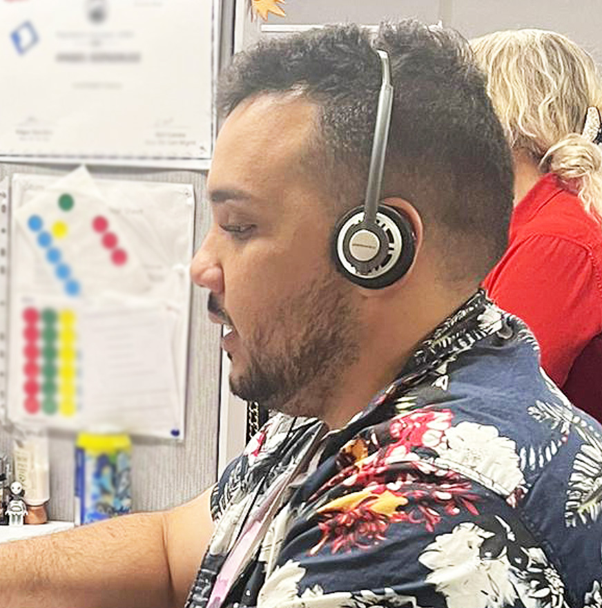 Black man sits at a computer with a headset on.