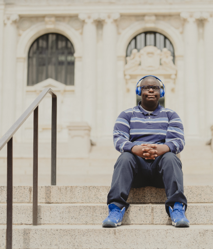 Black man with IDD sitting on steps outdoors